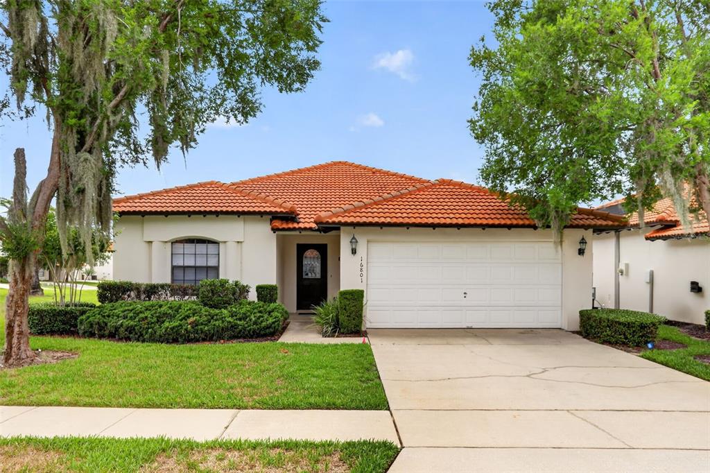 A single-story house with a white stucco exterior, orange tile roof, and a two-car garage — 16801 LAZY BREEZE LOOP, CLERMONT, FL