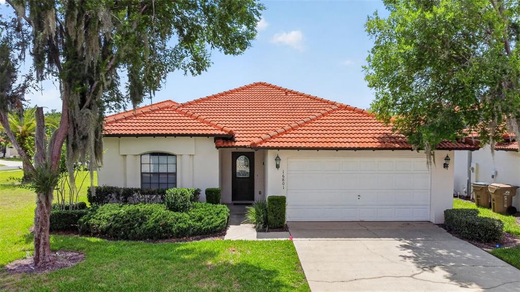 A single-story house with a red tile roof, white stucco walls, and a two-car garage — 16801 LAZY BREEZE LOOP, CLERMONT, FL