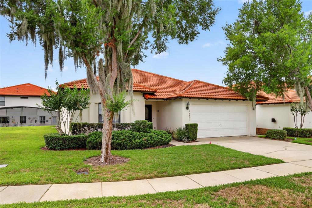 A single-story house with a white stucco exterior, orange tile roof, and a two-car garage — 16801 LAZY BREEZE LOOP, CLERMONT, FL