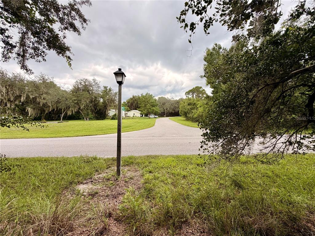 A paved road curves through a grassy, tree-lined residential area with a single street lamp — 5717 SUN VALLEY DRIVE, SEBRING, FL