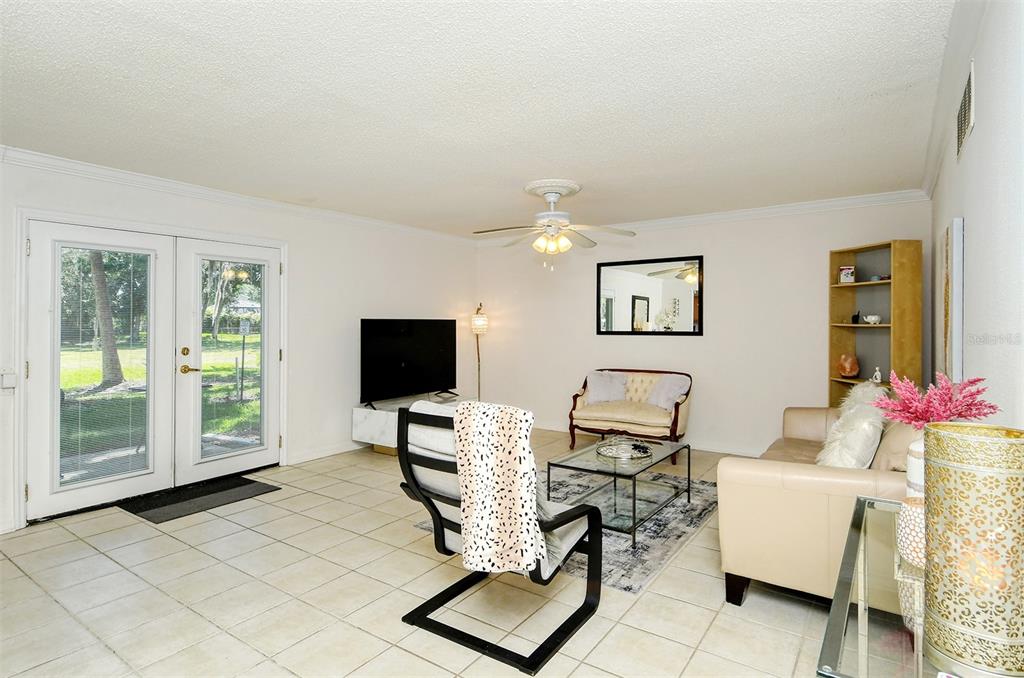 A living room features tile flooring, a ceiling fan, a television, and glass patio doors — 1877 TOUCAN WAY UNIT 400, SARASOTA, FL