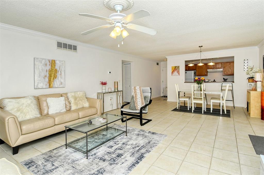 A living room with beige tile floors, a tan sofa, and an adjacent dining area — 1877 TOUCAN WAY UNIT 400, SARASOTA, FL