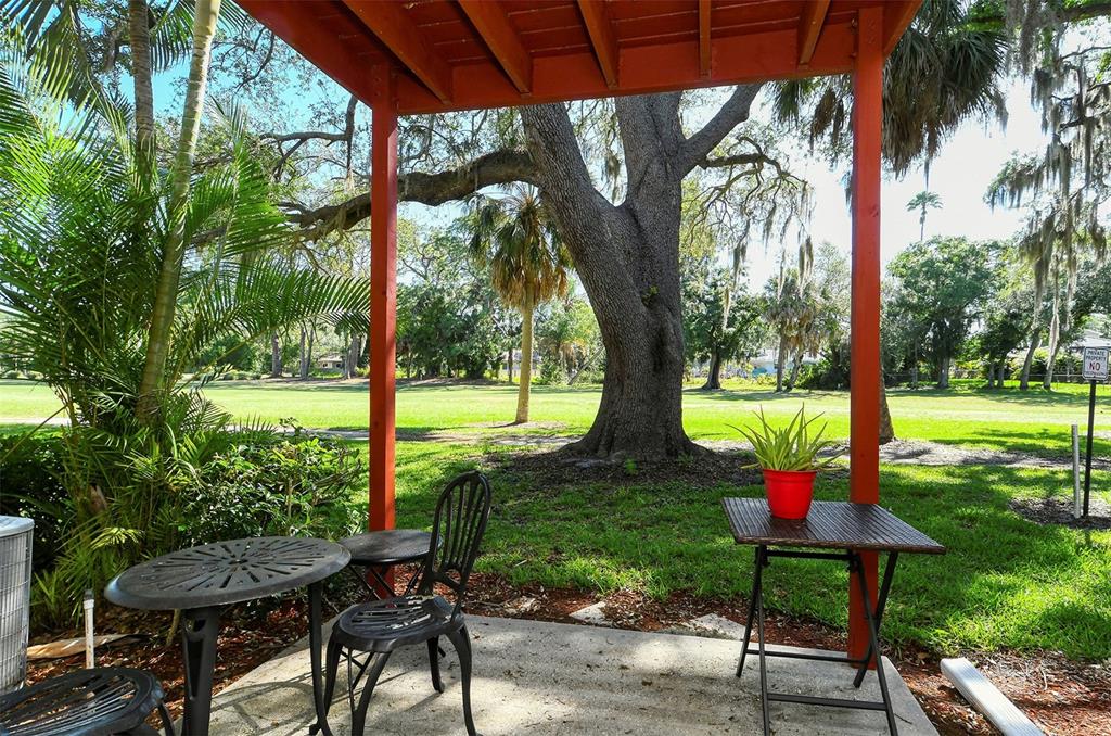 A patio with a red pergola, metal furniture, and a potted plant overlooking a lawn — 1877 TOUCAN WAY UNIT 400, SARASOTA, FL