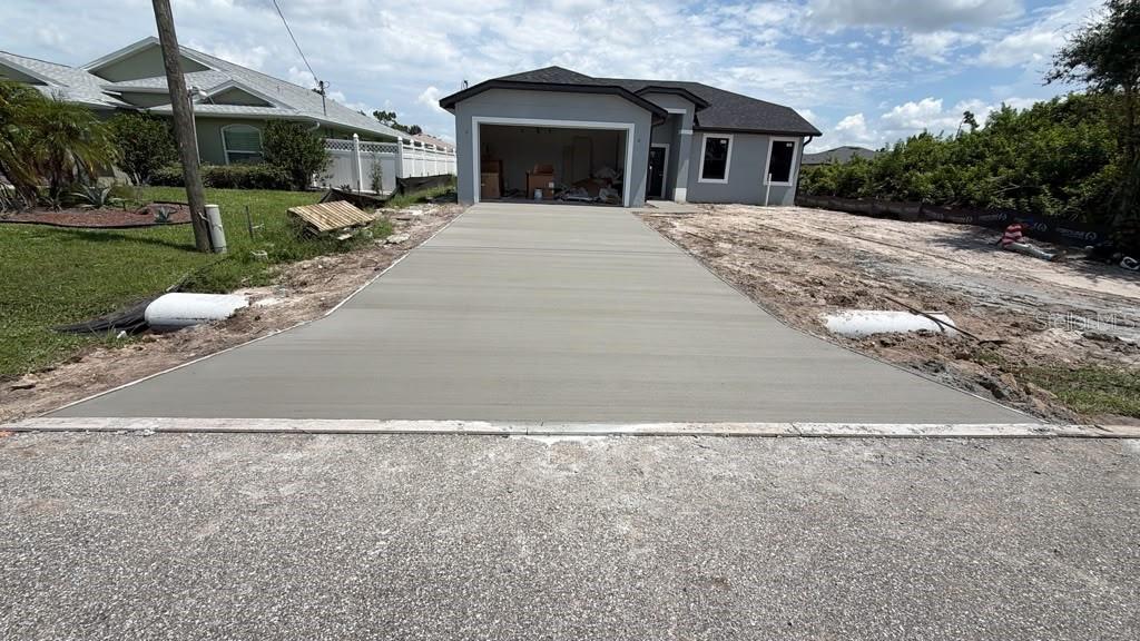 A newly poured concrete driveway leads to the garage of a single-story gray house — 122 GREEN OAK PARK, ROTONDA WEST, FL