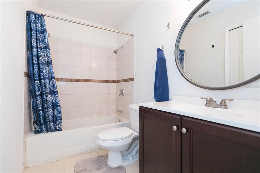 A bathroom features a dark wood vanity, a round mirror, and a shower-tub combination — 8636 MALLARD RESERVE DRIVE UNIT 201, TAMPA, FL
