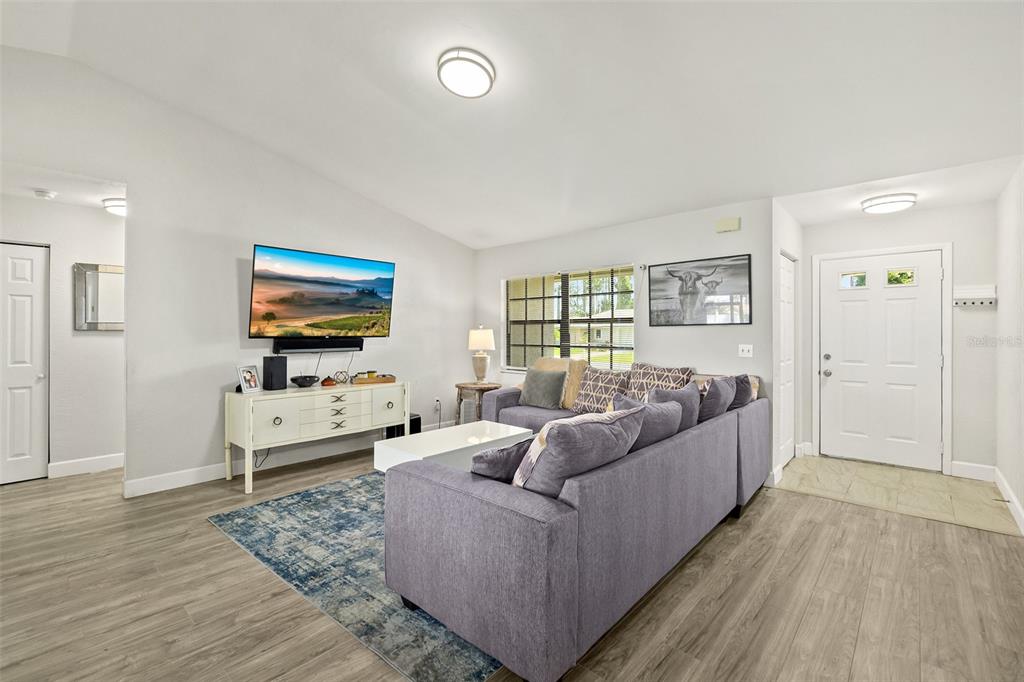 A living room features gray wood-look flooring, a sectional sofa, and a wall-mounted television — 14 BALLARD LANE, PALM COAST, FL