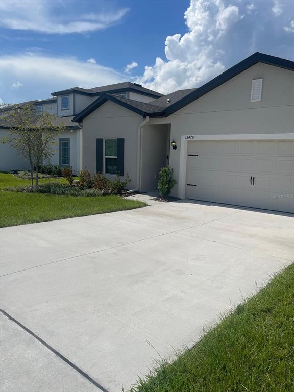A single-story house with a beige exterior, a two-car garage, and a concrete driveway — 13470 LEAPING WATER WAY, ASTATULA, FL