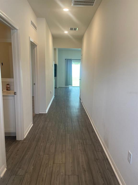 A hallway with wood-look tile flooring leads toward a room with a sliding glass door — 13470 LEAPING WATER WAY, ASTATULA, FL