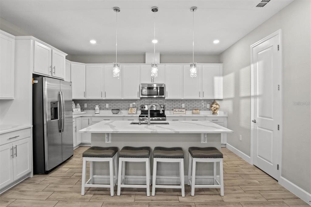 A modern kitchen features white cabinetry, a large marble-topped island with four stools, and stainless appliances — 1804 VISTA VIEW DRIVE, DUNDEE, FL