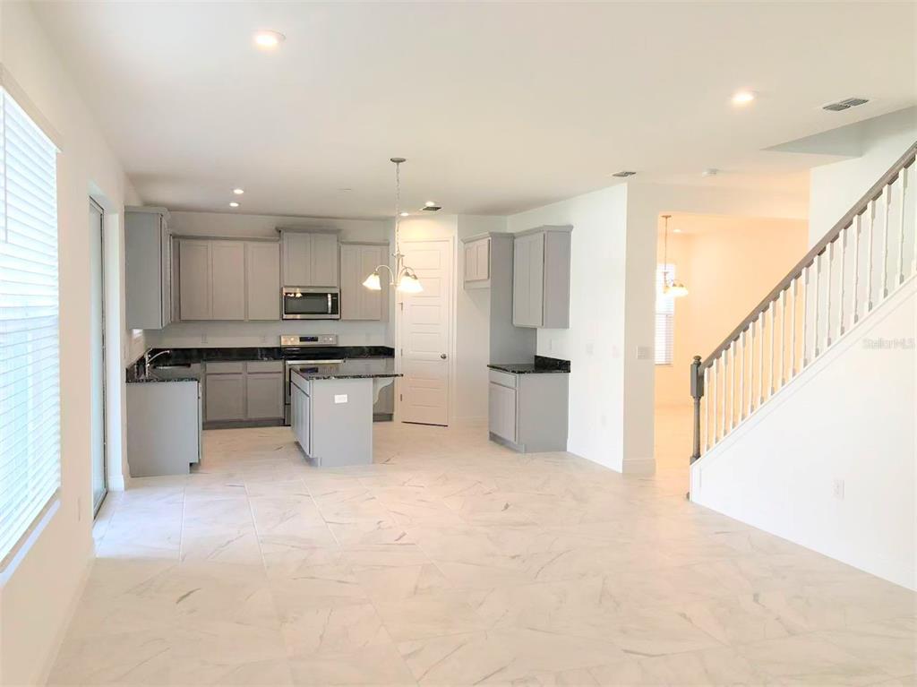 A kitchen with gray cabinets, dark countertops, and tile flooring next to a staircase — 2578 TRIELLE AVENUE, KISSIMMEE, FL