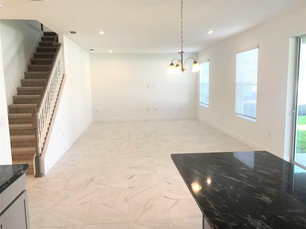 An open-concept living area features white tile floors, a carpeted staircase, and a dining chandelier — 2578 TRIELLE AVENUE, KISSIMMEE, FL