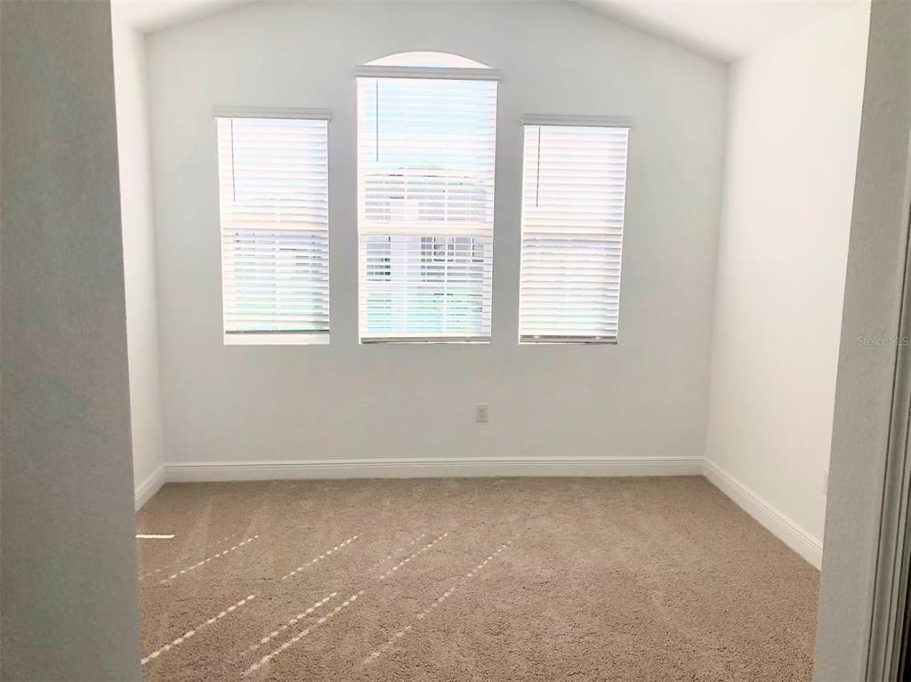 An empty room features beige carpet, white walls, and three windows with white blinds — 2578 TRIELLE AVENUE, KISSIMMEE, FL