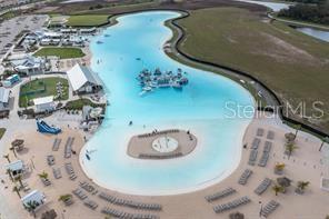 An aerial view shows a large turquoise swimming lagoon with a central island and beach — 17066 OVAL RUM DRIVE, WIMAUMA, FL