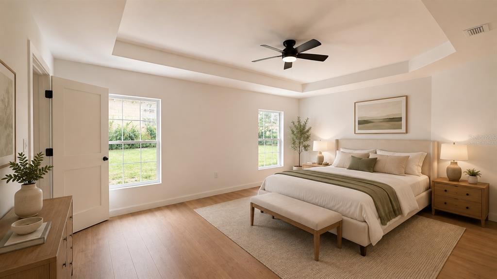 A bedroom with light wood floors, a tray ceiling, a ceiling fan, and a bed — 644 and 646 E FRANKLIN STREET, OVIEDO, FL