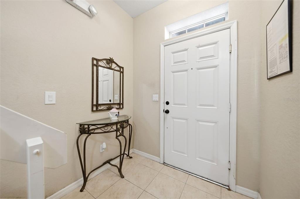 An entryway features a white front door, a metal console table, and a wall mirror — 2402 CARAVELLE CIRCLE, KISSIMMEE, FL