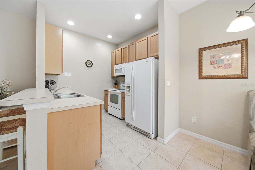 A kitchen features light wood cabinets, white appliances, tile flooring, and a breakfast bar — 2402 CARAVELLE CIRCLE, KISSIMMEE, FL