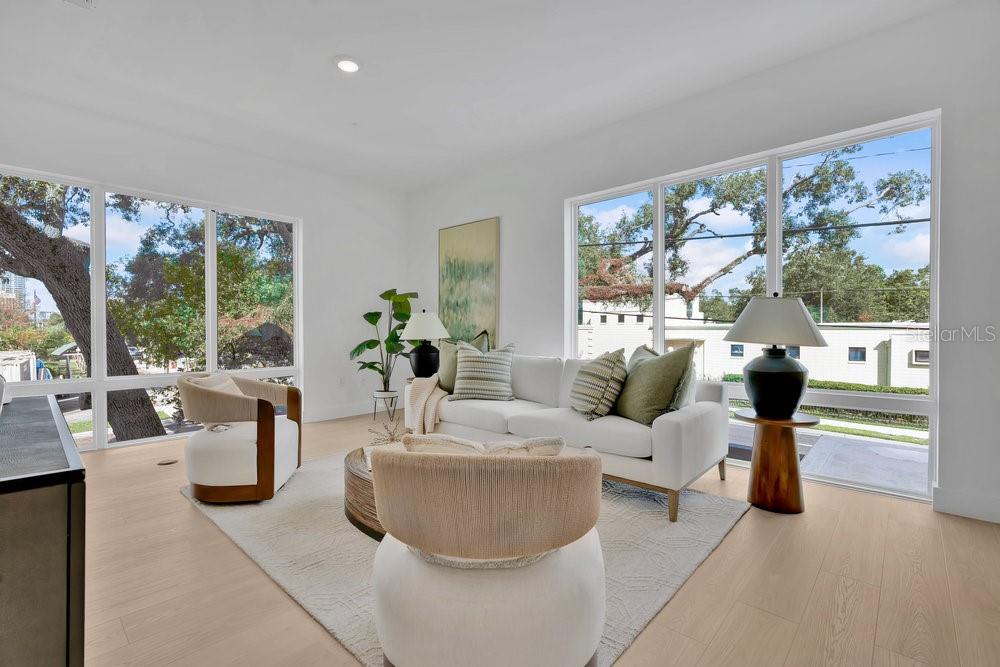 A bright living room features white walls, light wood floors, and large windows with outdoor views — 1010 E ROBINSON STREET, ORLANDO, FL