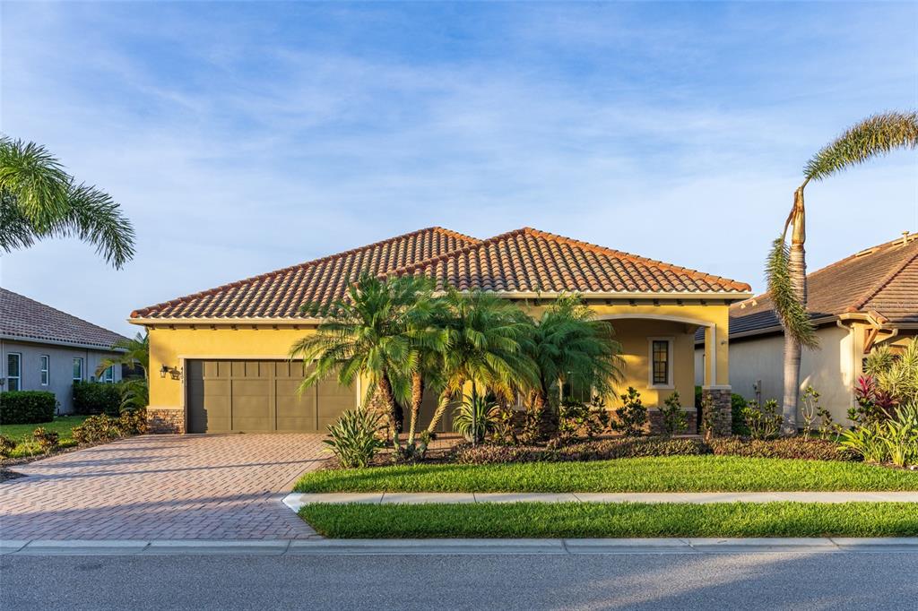 A yellow single-story house with a tile roof, palm trees, and a paved driveway — 4703 TOBERMORY WAY, BRADENTON, FL