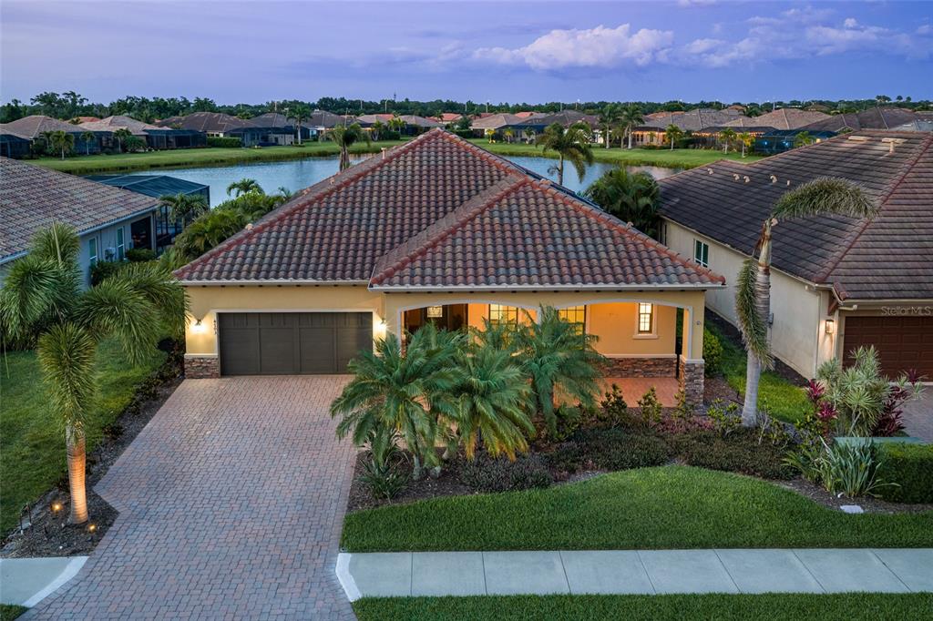 An aerial view of a single-story house with a tile roof, driveway, and lakefront backyard — 4703 TOBERMORY WAY, BRADENTON, FL
