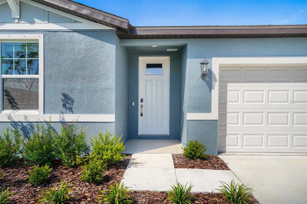 A blue house exterior features a white front door, a garage, and a landscaped yard — 7705 SATTERFIELD TERRACE, PARRISH, FL