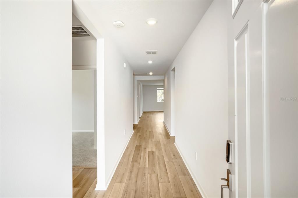 A long hallway with light wood-look flooring leads toward a window at the far end — 7705 SATTERFIELD TERRACE, PARRISH, FL