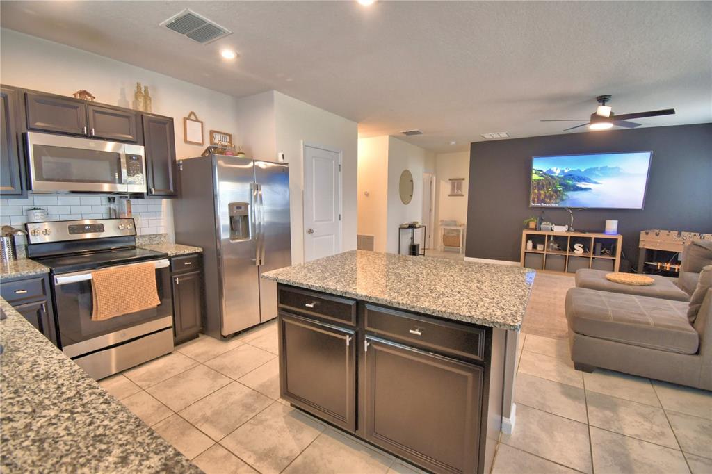 A kitchen with dark cabinets and granite countertops opens into a living area with a television — 542 EAGLE LANDING BOULEVARD, WINTER HAVEN, FL