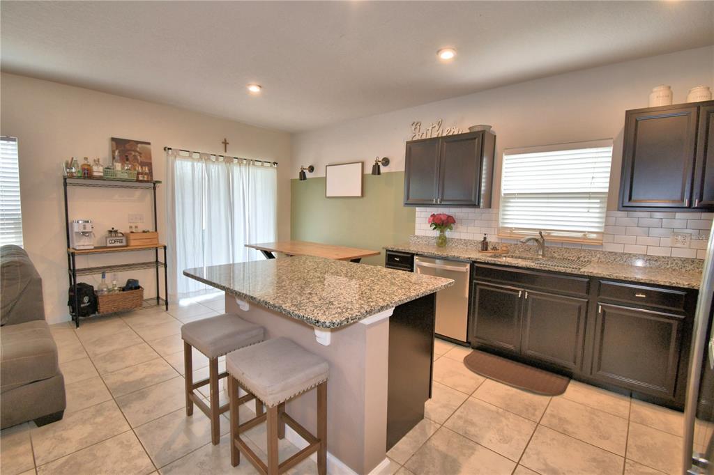 A kitchen features dark cabinets, granite countertops, a central island with stools, and tile flooring — 542 EAGLE LANDING BOULEVARD, WINTER HAVEN, FL