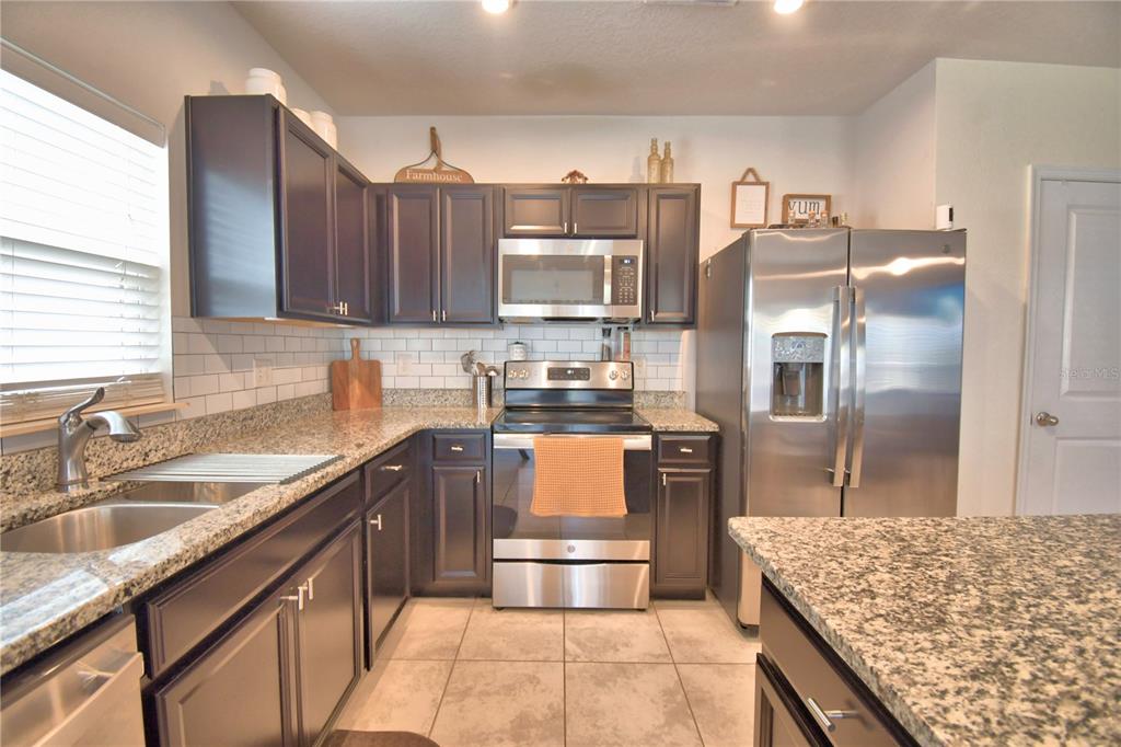A kitchen features dark wood cabinets, granite countertops, stainless steel appliances, and a tile backsplash — 542 EAGLE LANDING BOULEVARD, WINTER HAVEN, FL