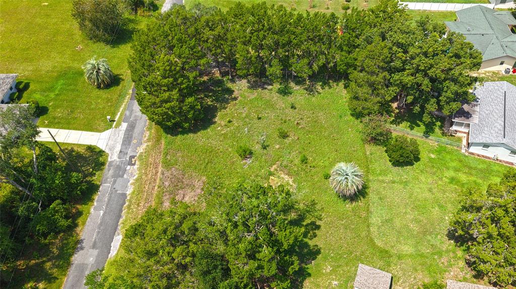 An aerial view shows a vacant, grassy residential lot bordered by trees and neighboring houses — 3577 E KIRBY LANE, INVERNESS, FL