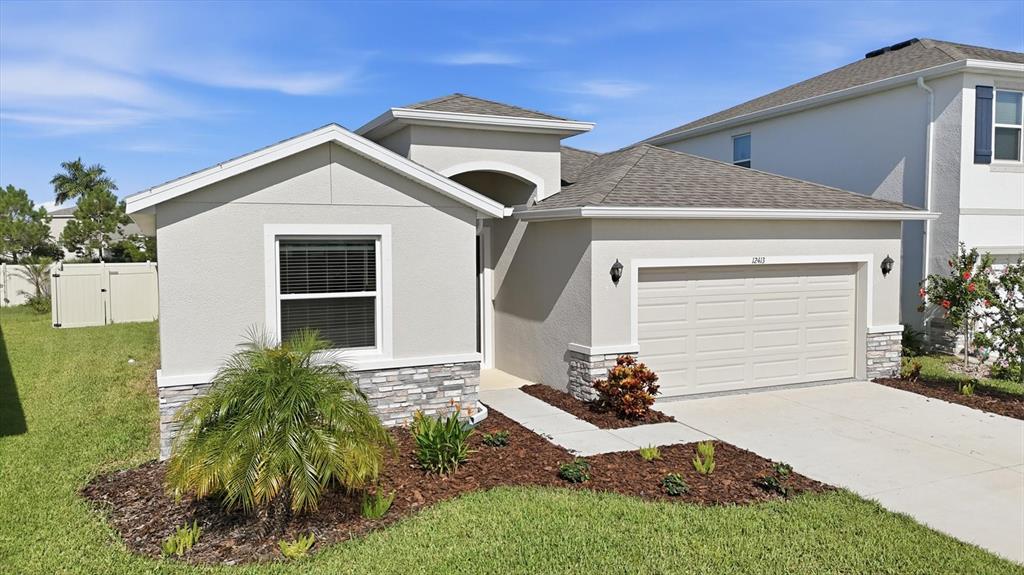A single-story house with a beige stucco exterior, stone accents, and a two-car garage — 12413 DORA TRAIL, PARRISH, FL