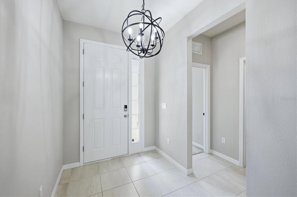 A bright entryway features a modern orb chandelier, white door, and light-colored tile flooring — 12413 DORA TRAIL, PARRISH, FL