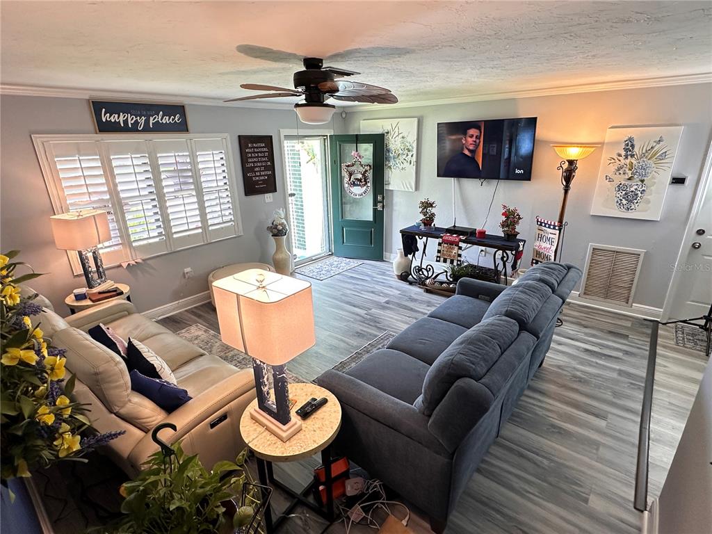 A living room features gray wood-look flooring, a ceiling fan, and two sofas facing a television — 9470 JOEL DRIVE, SEMINOLE, FL