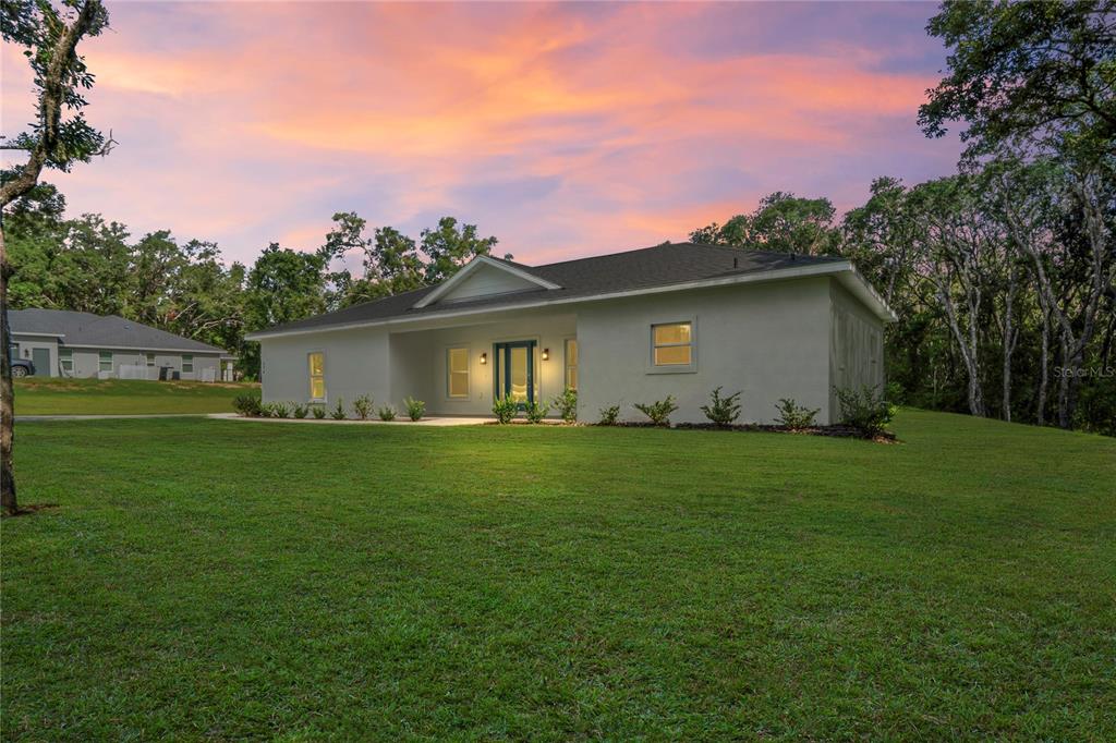 A single-story house with a light-colored exterior sits on a grassy lawn at sunset — 279 W PEARSON STREET, HERNANDO, FL