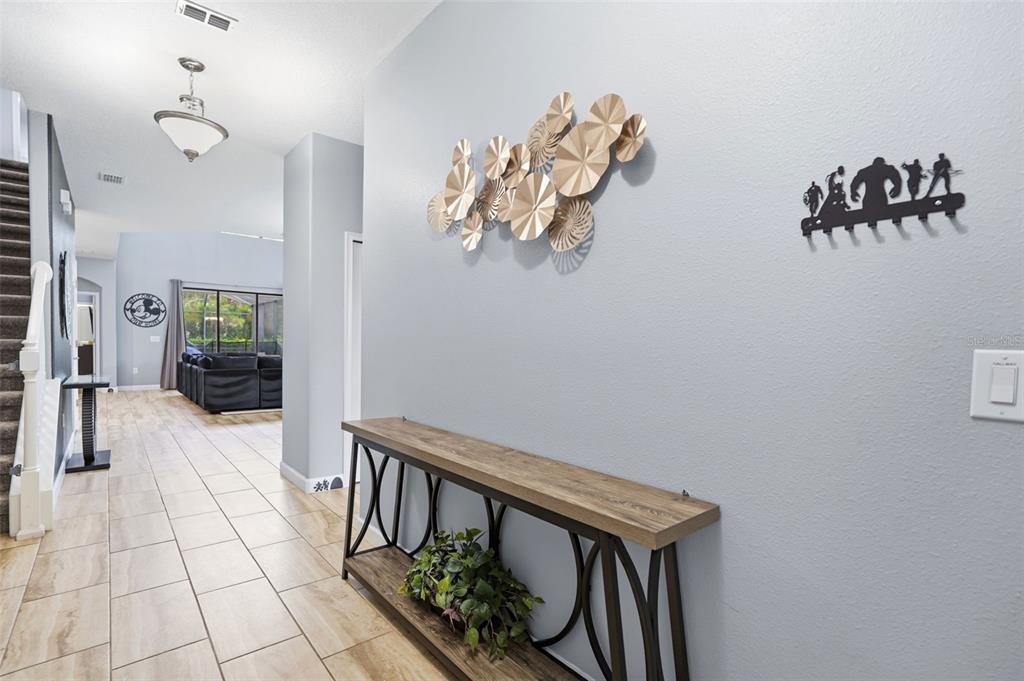 A hallway features a wooden console table, gold wall art, and a black superhero-themed coat rack — 5439 SOLTERRA CIRCLE, DAVENPORT, FL
