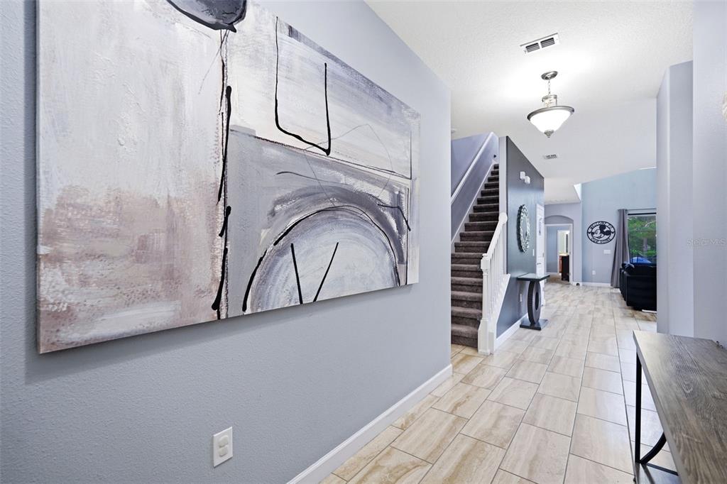 A hallway features light-colored tile flooring, a large abstract painting, and a staircase with carpet — 5439 SOLTERRA CIRCLE, DAVENPORT, FL