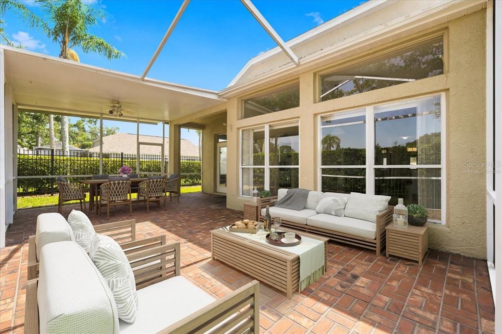 A covered patio with a brick floor and screened-in walls overlooks a fenced backyard — 4628 CORSAGE DRIVE, LUTZ, FL