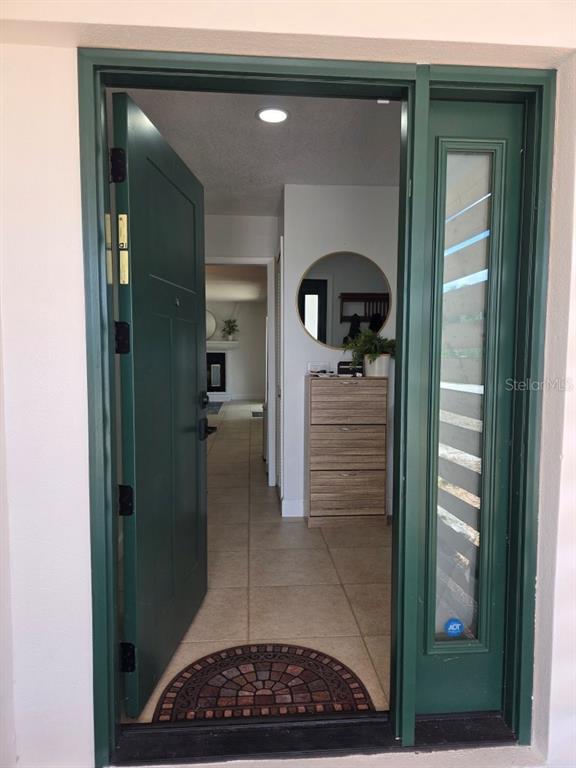 An open green front door reveals a tiled entryway with a wooden shoe cabinet and mirror — 7005 TALBOT DR, ORLANDO, FL
