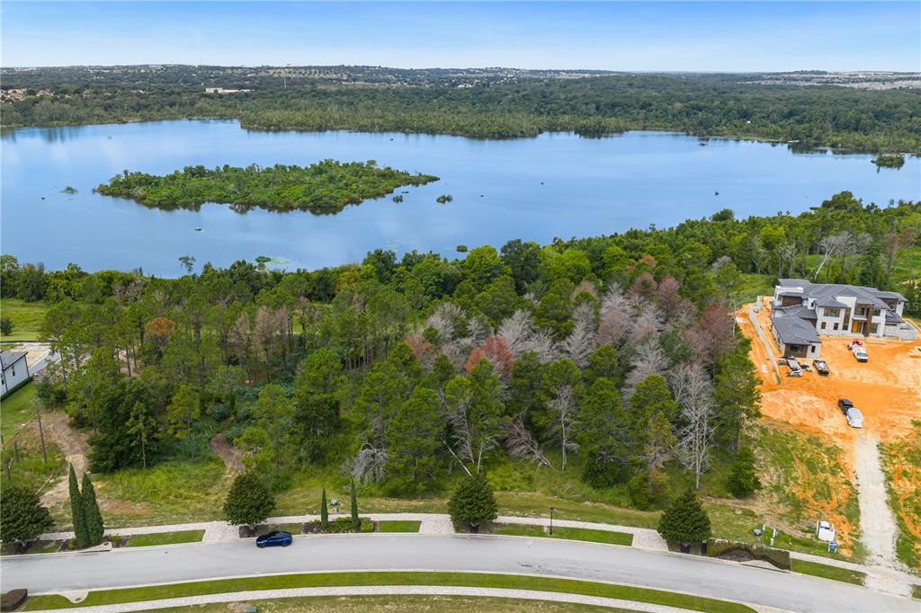 An aerial view shows a vacant wooded lot situated between a lake and a house — 16409 PENDIO DRIVE, MONTVERDE, FL