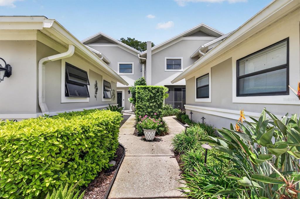 A concrete walkway leads between two light-colored buildings with manicured hedges and landscaping — 2631 ROYAL LIVERPOOL DRIVE, TARPON SPRINGS, FL