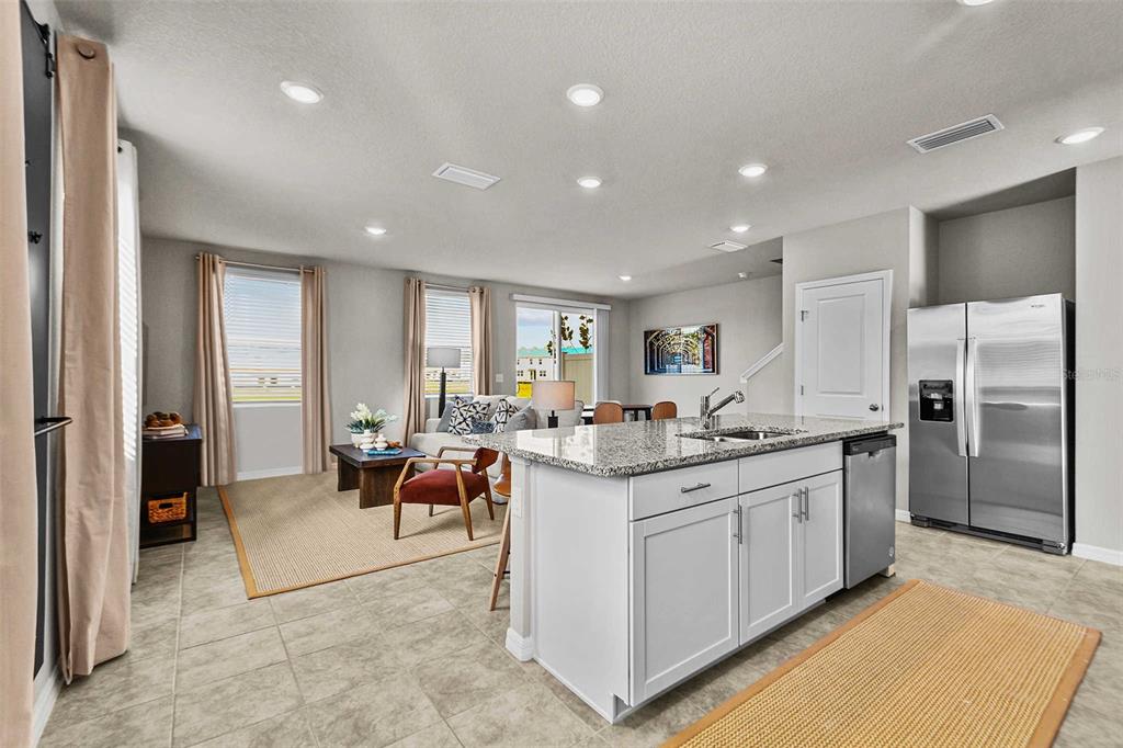 A kitchen with a granite island and stainless steel refrigerator opens into a living area — 8683 HOLLY GROVE COURT UNIT Oakville, RIVERVIEW, FL