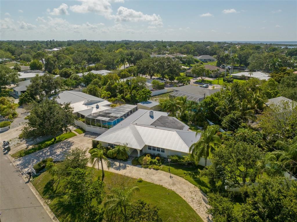 An aerial view shows a single-story house with a metal roof and a screened pool — 7202 18TH AVENUE NW, BRADENTON, FL