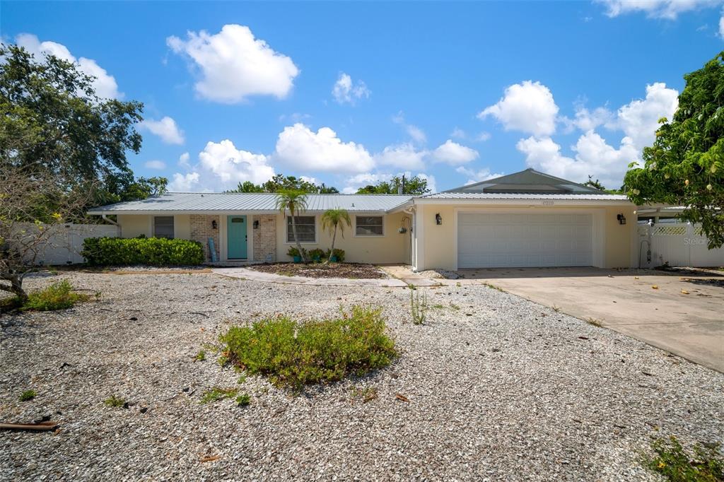 A single-story house with a light yellow exterior, metal roof, and a gravel front yard — 7202 18TH AVENUE NW, BRADENTON, FL