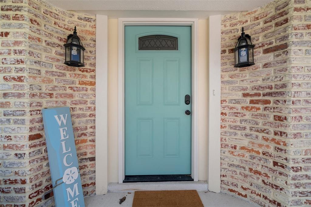 A teal front door is flanked by two black lanterns on a brick exterior wall — 7202 18TH AVENUE NW, BRADENTON, FL