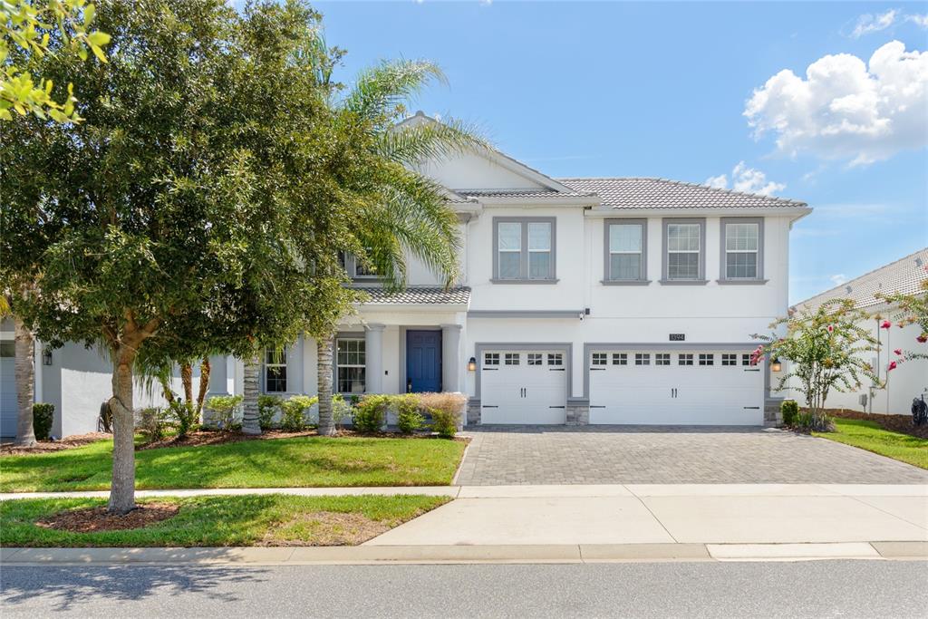 A two-story house with a paved driveway, three-car garage, and a palm tree at sunset — 1394 OLYMPIC CLUB BOULEVARD, CHAMPIONS GATE, FL