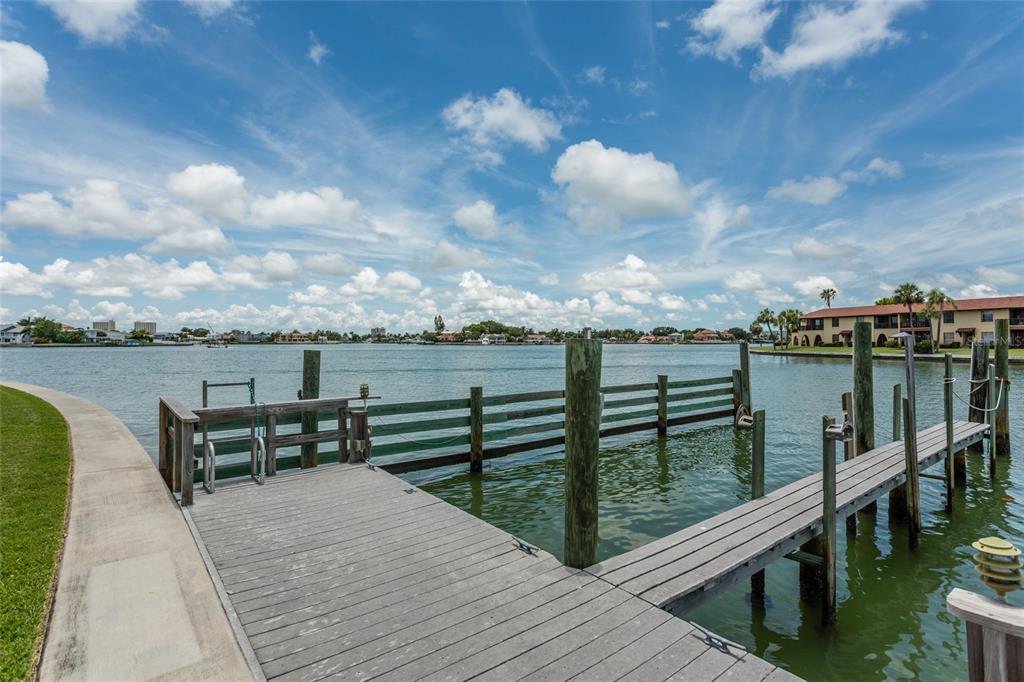A wooden dock extends into a calm bay with a concrete walkway and distant buildings — 505 SANDY HOOK ROAD UNIT 505, TREASURE ISLAND, FL