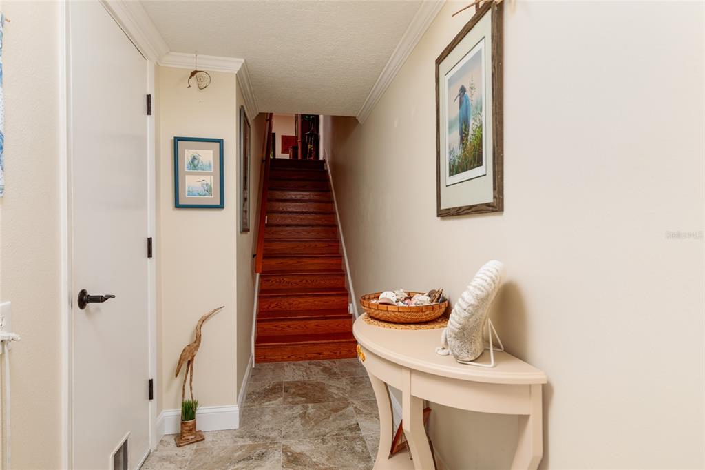 A hallway features a wooden staircase, tile flooring, a console table, and framed wall art — 505 SANDY HOOK ROAD UNIT 505, TREASURE ISLAND, FL