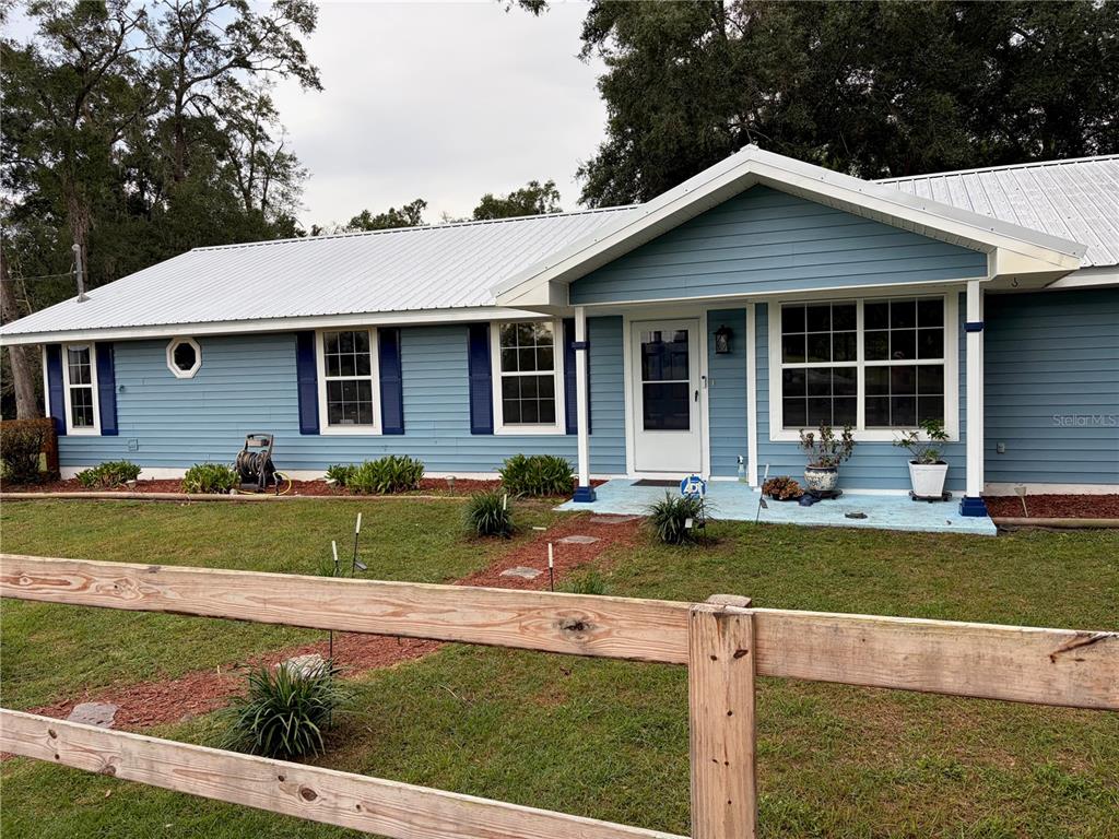 A blue single-story house with a metal roof sits behind a wooden split-rail fence — 1890 NW 167TH PLACE, TRENTON, FL