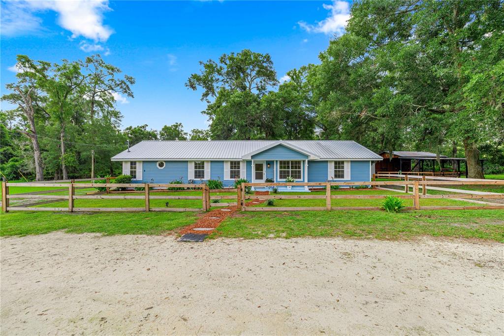 A blue single-story house with a metal roof sits behind a wooden fence — 1890 NW 167TH PLACE, TRENTON, FL