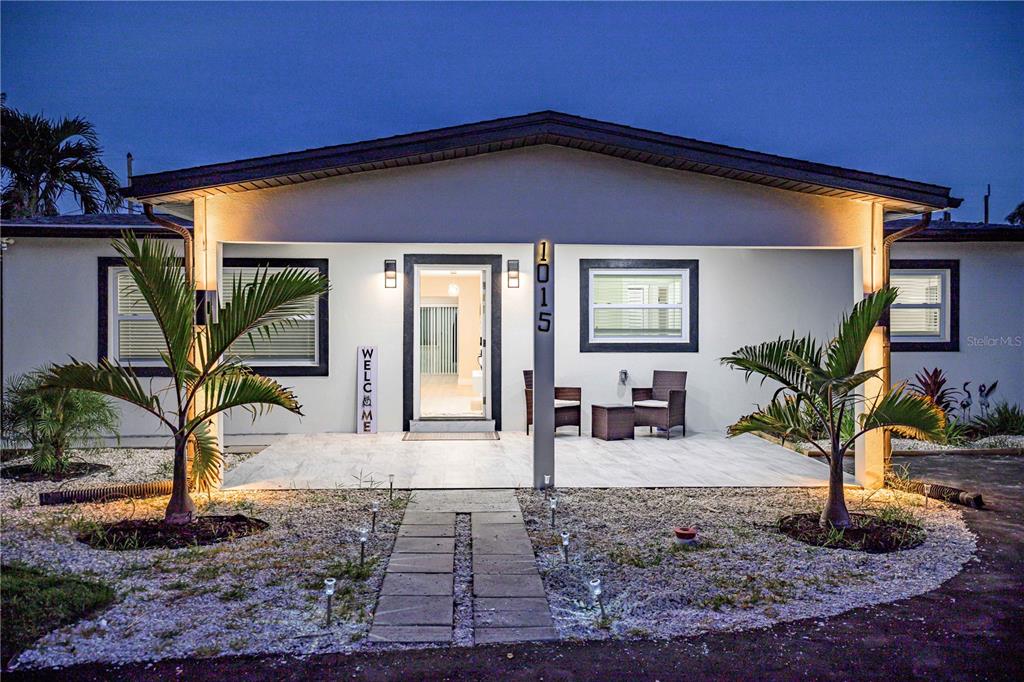 A single-story white house features a covered front porch, palm trees, and a gravel yard — 1015 BOCA CIEGA ISLE DRIVE, ST PETE BEACH, FL