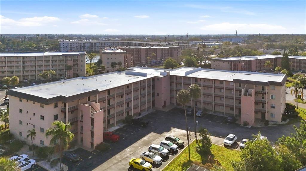 An aerial view shows a multi-story apartment complex with a parking lot and surrounding trees — 4143 HERON WAY 207 BLDG E, BRADENTON, FL